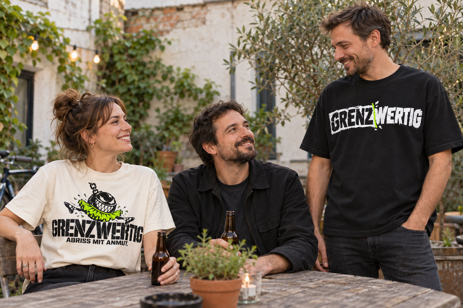 Inszeniertes Tragebild: drei Freunde im Innenhof, mit schwarzem Original-Logo-Shirt und cremefarbenem Abriss-mit-Anmut-Shirt